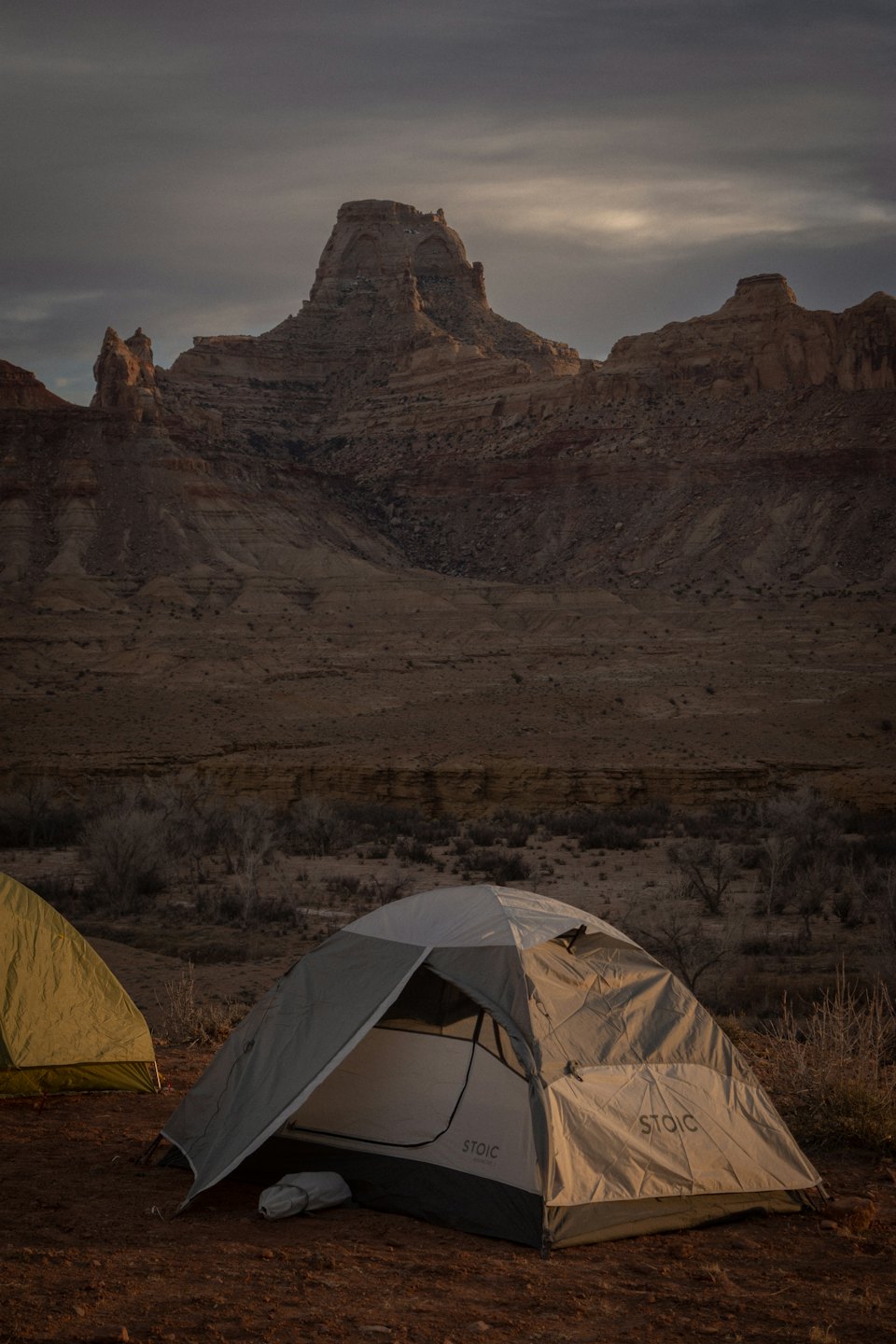 Two camping tents sit on desert ground before rock formations.