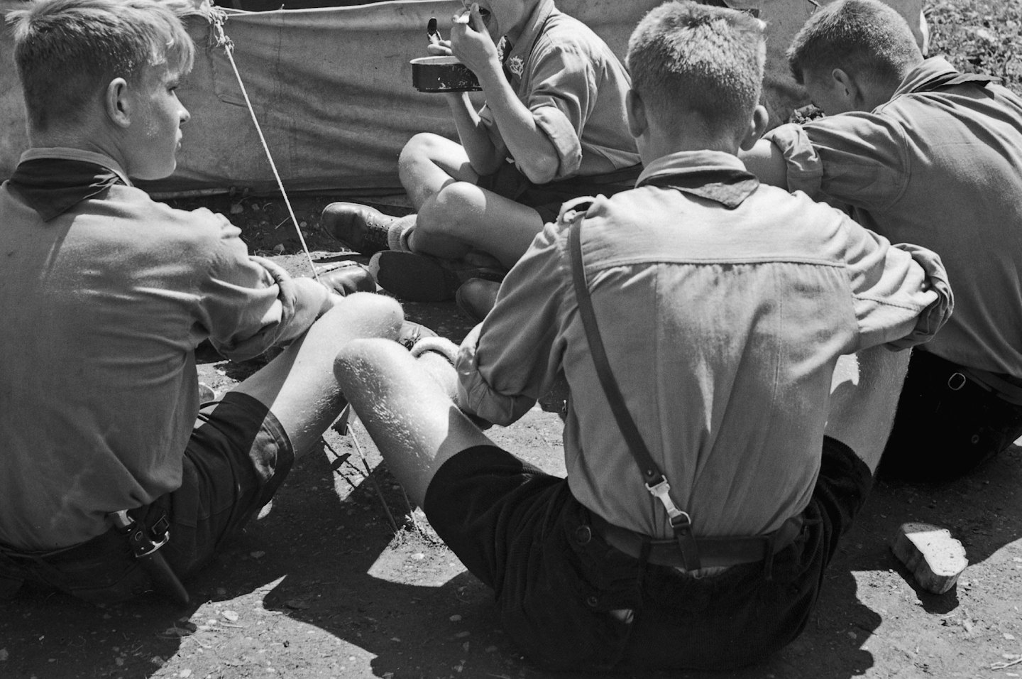 Four scouts sitting on the ground outside a canvas tent.
