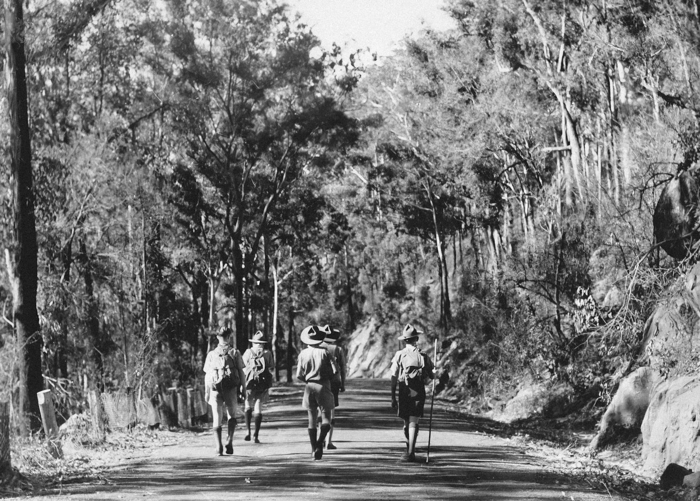 Scouts with backpacks walk along a dirt forest path.