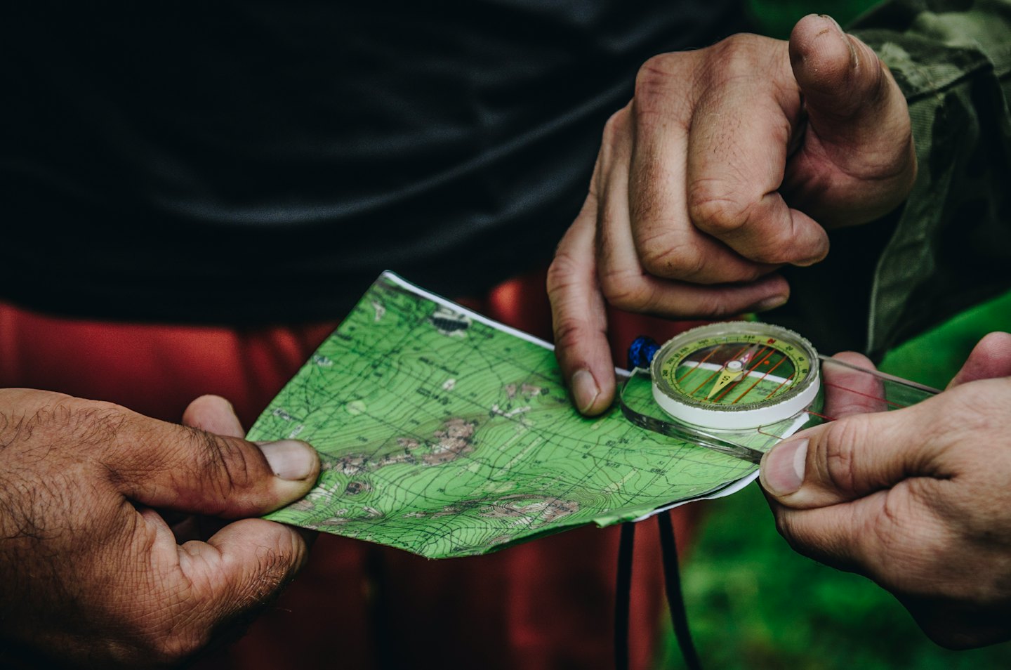Hands studying a topographical map and compass outdoors.